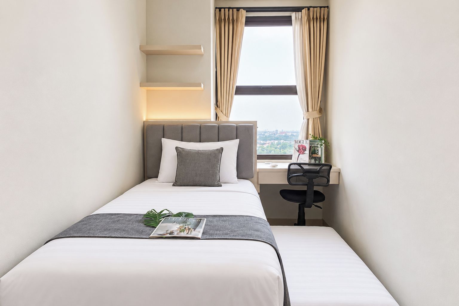 A hotel room with a bed, a desk, a chair, a window with curtains, and a magazine on the bed.