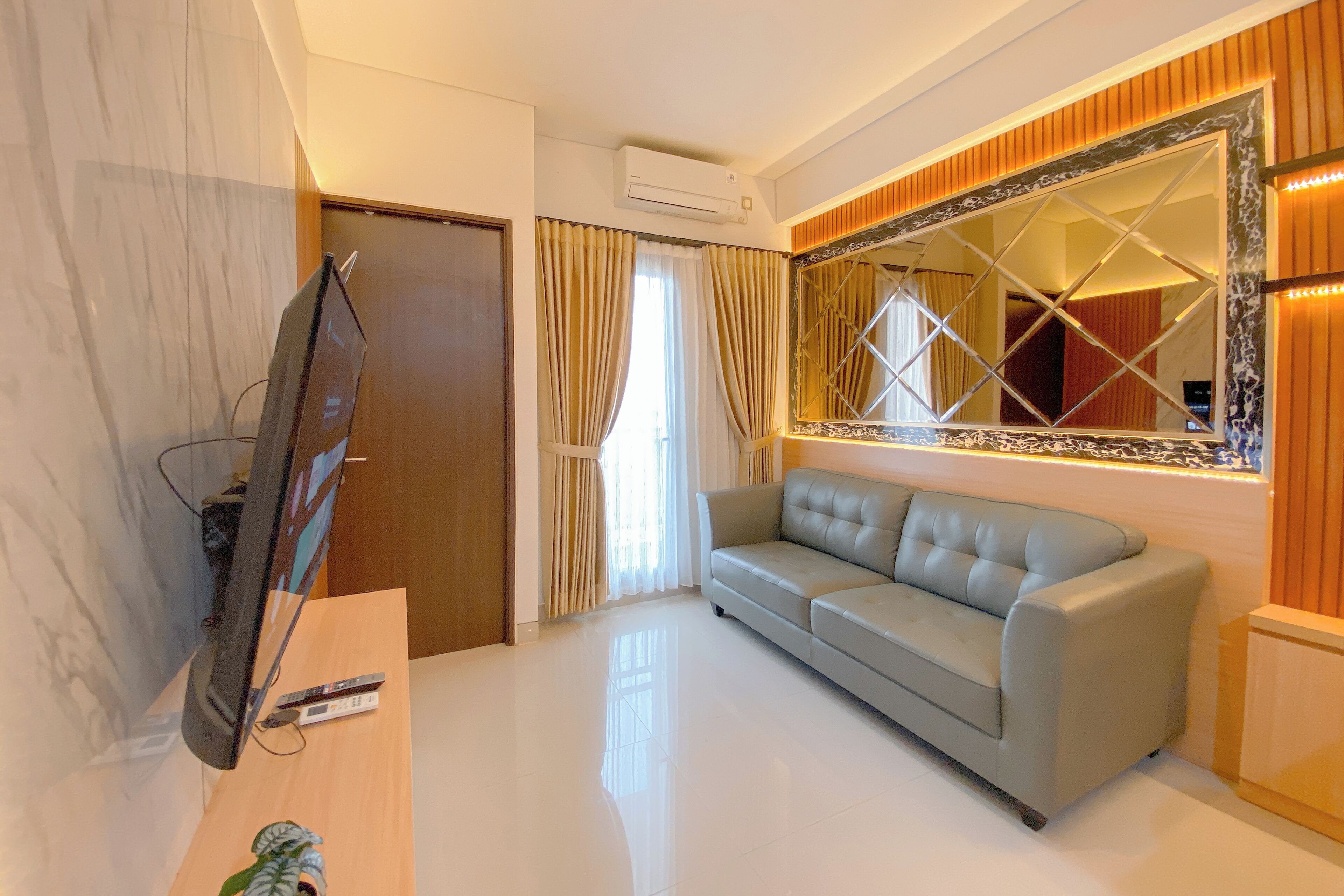 A modern living room with a flat-screen TV, a sofa, a wooden cabinet, and a large decorative mirror.