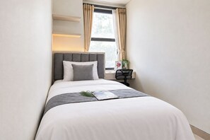 A neatly made bed with a grey headboard, a bedside table with a magazine, and a window with curtains. - Cozy And Good Place 2Br Transpark Cibubur Apartment (Depok)