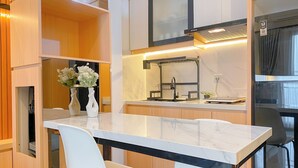 A modern kitchen with a white marble countertop, two white chairs, a black faucet, and a small potted plant. - Cozy And Good Place 2Br Transpark Cibubur Apartment (Depok)