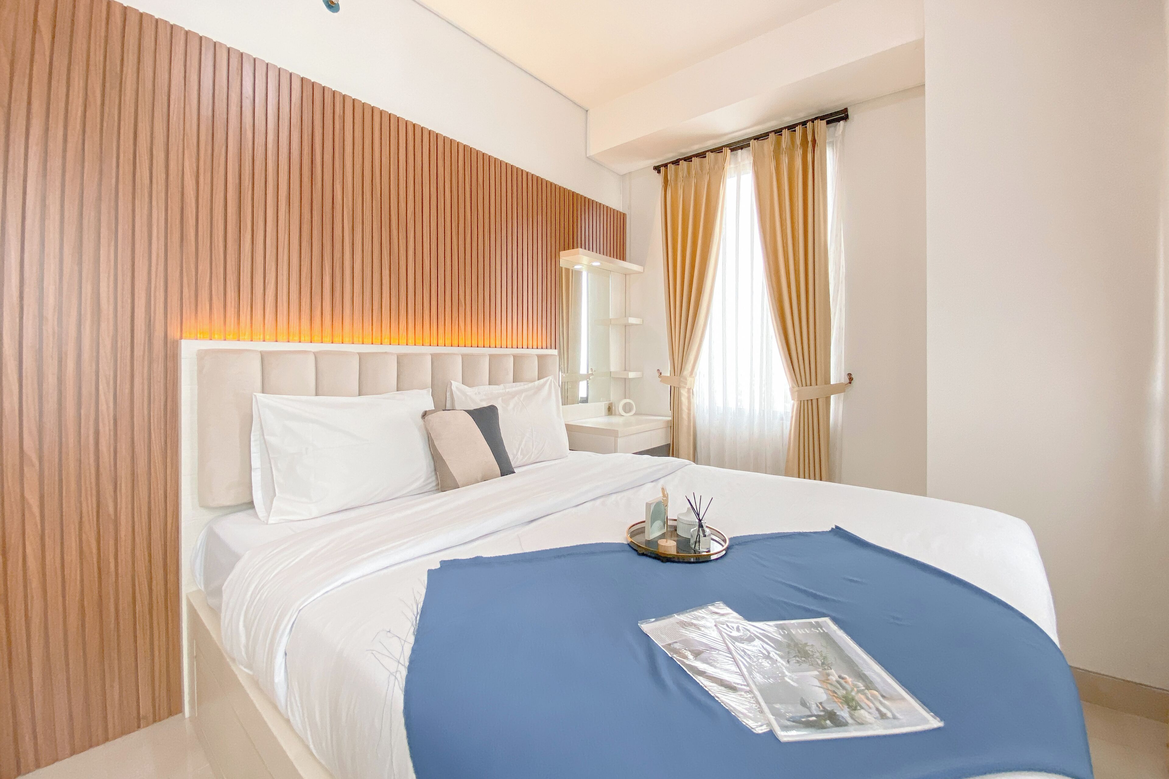 A modern hotel room with a large bed, wooden panel wall, and a bedside table with a lamp.