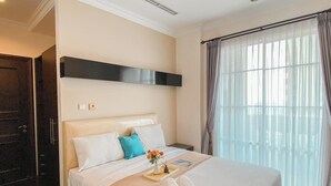 A hotel room with a bed, a bedside table, a window with curtains, and a door. - Spacious And Modern Look 3Br Bellezza Apartment (Jakarta)