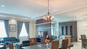 A modern living room with a glass dining table, comfortable seating, a television, and a chandelier. - Spacious And Modern Look 3Br Bellezza Apartment (Jakarta)