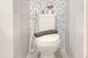 A toilet with a rolled towel, a flower vase, and a showerhead. - Cozy And Simply Studio Room At Apartment Tokyo Riverside Pik 2 (Teluknaga)
