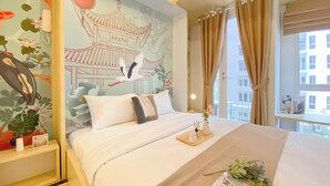 A neatly made bed with a magazine and flowers, a wall mural, and a window with curtains. - Affordable And Homey Studio At Tokyo Riverside Pik 2 Apartment (Teluknaga)