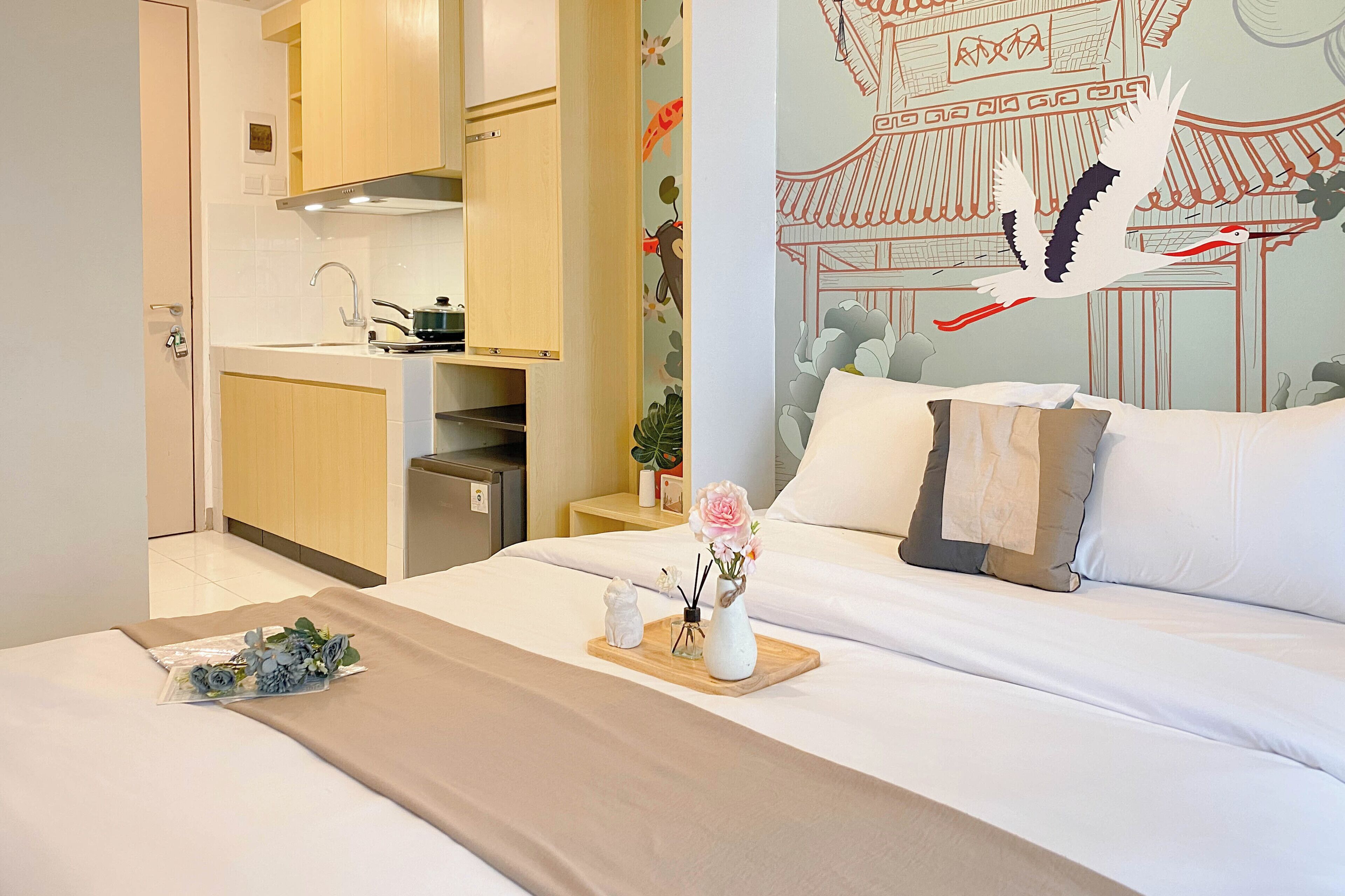 A hotel room with a bed, a wooden side table with a vase of flowers, a small statue, and a decorative wall mural.