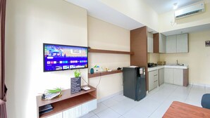 A modern living room with a flat-screen TV mounted on the wall, a wooden coffee table with a plant, and a black refrigerator. - Minimalist And Cozy 1Br Casa De Parco Apartment (Pagedangan)
