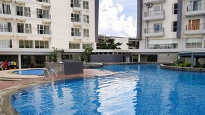 A swimming pool surrounded by a modern building with multiple balconies and windows. - Minimalist And Cozy 1Br Casa De Parco Apartment (Pagedangan)