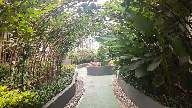 A pathway flanked by lush greenery and a bamboo archway leading to a building. - Minimalist And Cozy 1Br Casa De Parco Apartment (Pagedangan)