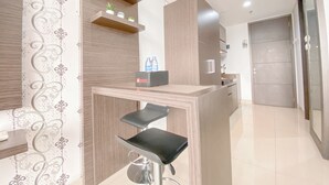 A modern kitchen with wooden cabinets, a countertop, and a bar stool. - Tranquil Studio Room At Dago Suites Apartment (Bandung)
