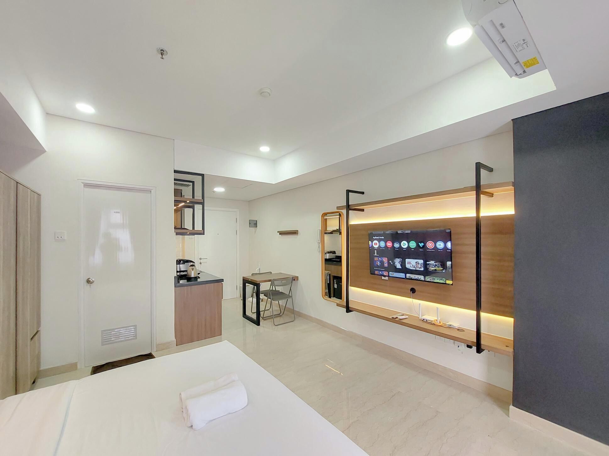 Une chambre d’hôtel moderne équipée d’un lit, d’un bureau, d’un téléviseur fixé au mur et d’une petite kitchenette.