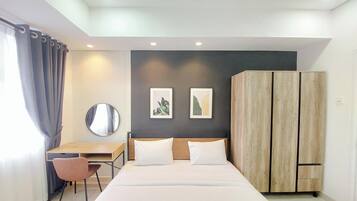 A modern hotel room with a large bed, a desk with a chair, a wardrobe, and two framed pictures on the wall.