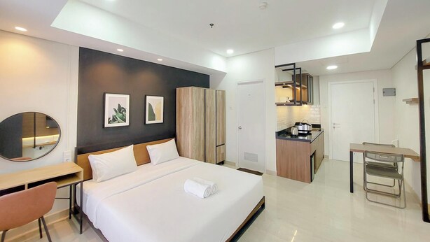Una habitación de hotel moderna con cama, escritorio, silla, espejo y kitchenette.