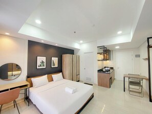 A modern hotel room with a bed, a desk, a chair, a mirror, and a kitchenette. - Relaxing Studio At Podomoro City Deli Medan Apartment (Medan)