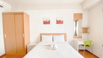 A bedroom with a bed, a wooden wardrobe, a desk, and two wall-mounted artworks.