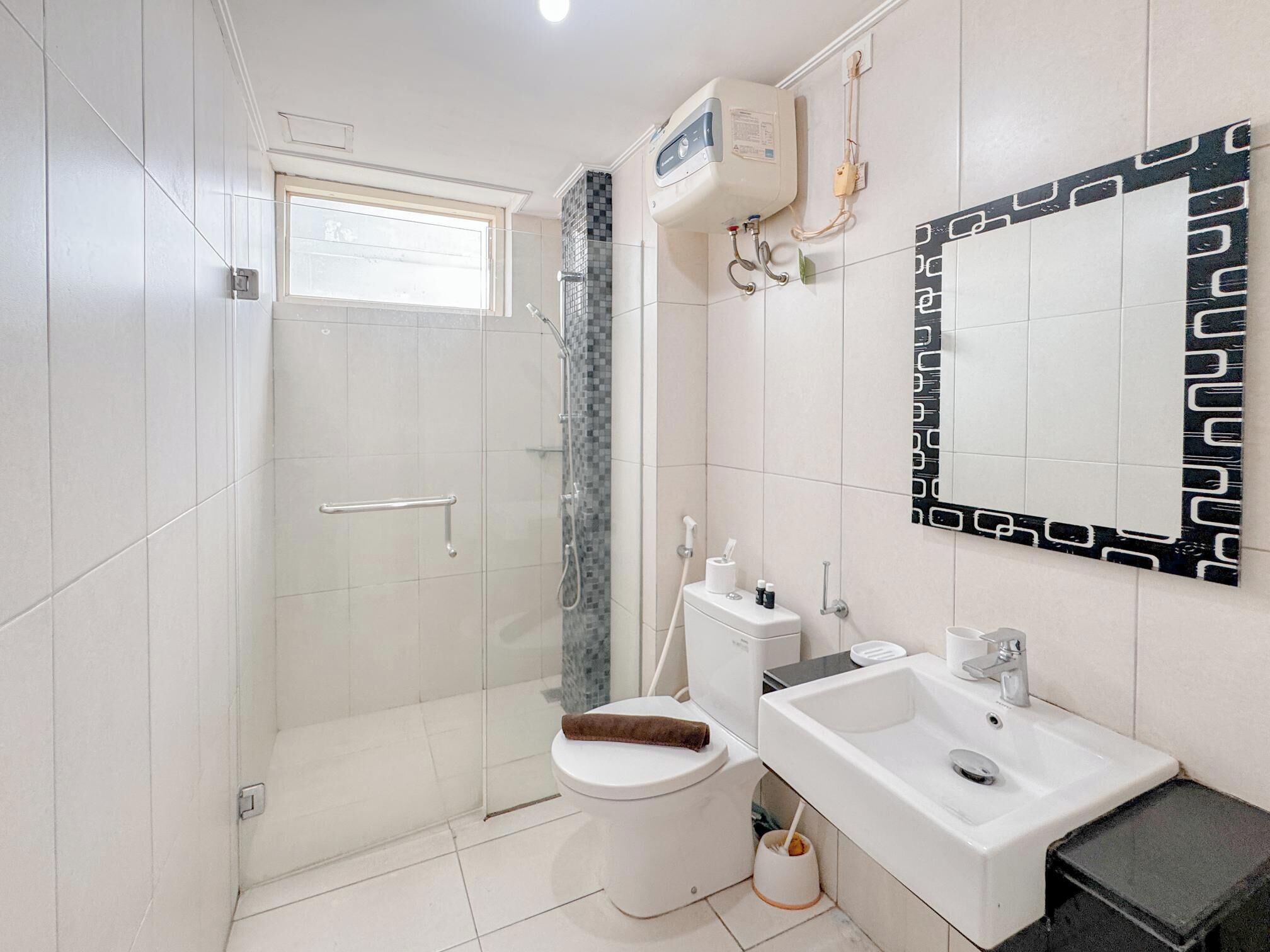 Une salle de bain moderne dotée d’une douche à parois de verre, de toilettes, d’un lavabo et d’un miroir encadré d’un motif géométrique.