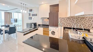 A modern kitchen with a central island, built-in appliances, and a dining area with a glass table. - Restful And Simple 2Br At The Via And The Vue Apartment (Surabaya)