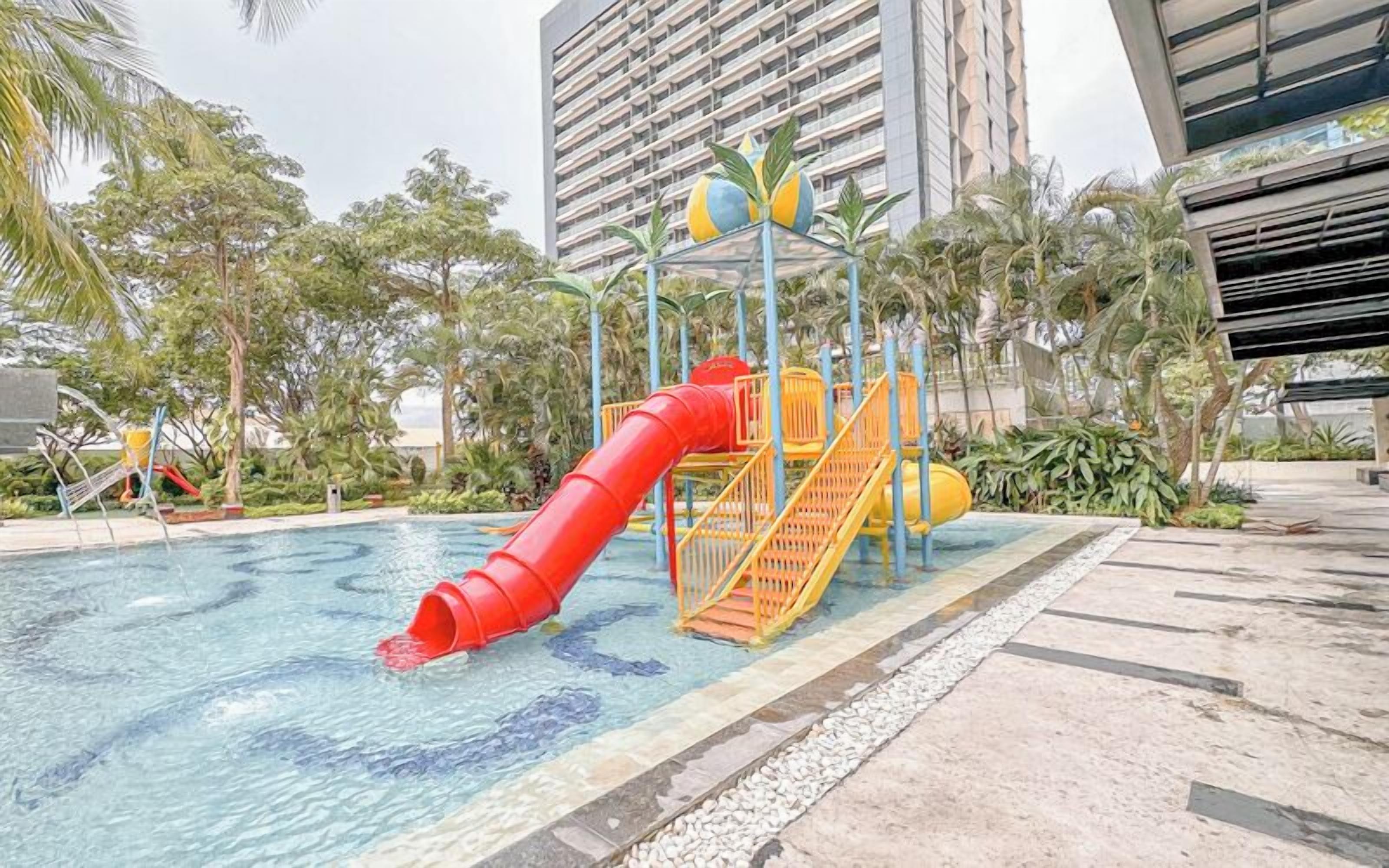 A swimming pool with a red slide and a yellow water play structure.