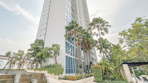 A tall, modern building with large windows and a series of palm trees in front. - Restful And Simple 2Br At The Via And The Vue Apartment (Surabaya)