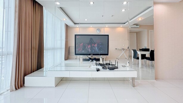 A modern hotel room with a large flat-screen TV, a glass coffee table, and a dining area with a white table and black chairs. - Restful And Simple 2Br At The Via And The Vue Apartment (Surabaya)