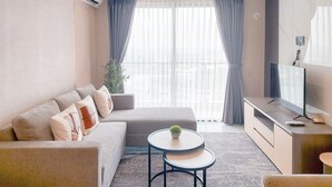 Un soggiorno moderno con un divano, un tavolino tondo con una pianta, una TV su un mobile e una grande finestra con tende.