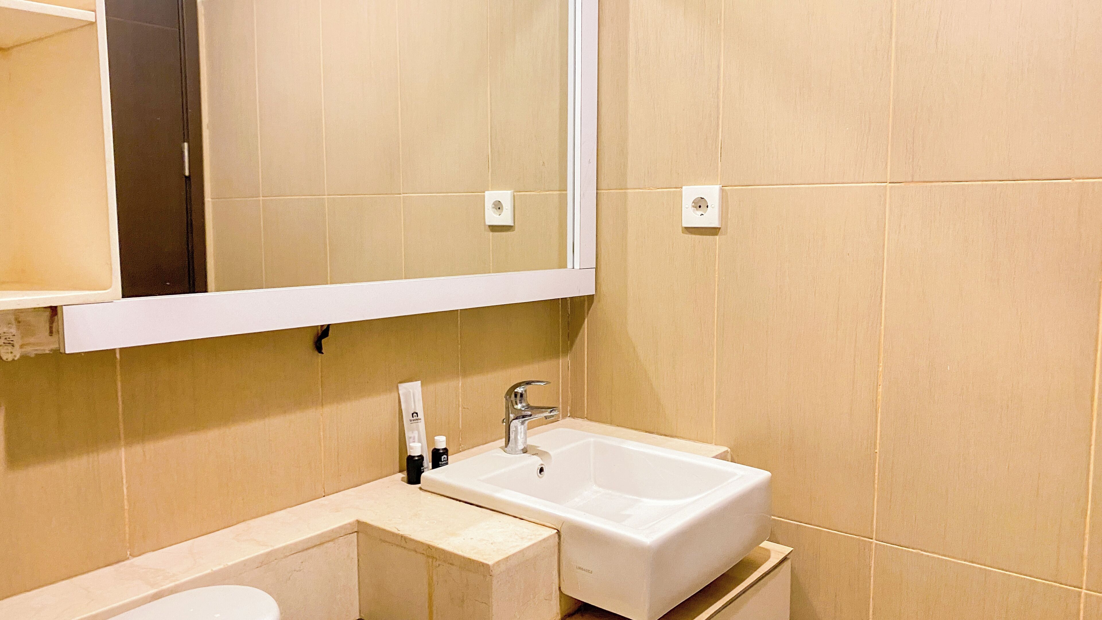 A bathroom with a white sink, a mirror above it, and beige tiled walls.
