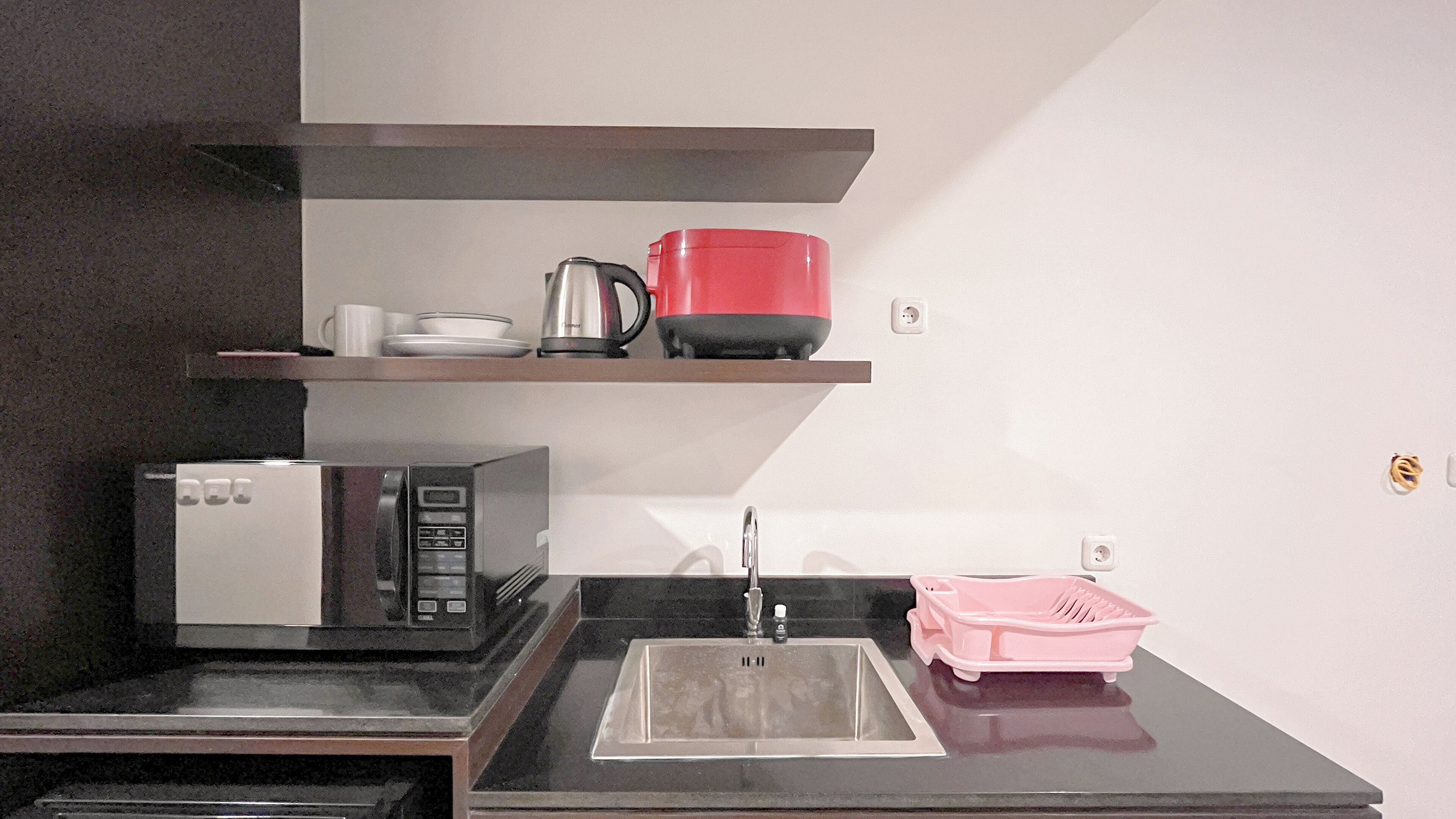 Cocina pequeña equipada con microondas, un lavamanos y una tetera roja sobre una repisa.