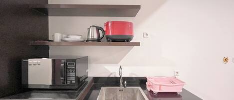 Cocina pequeña equipada con microondas, un lavamanos y una tetera roja sobre una repisa.