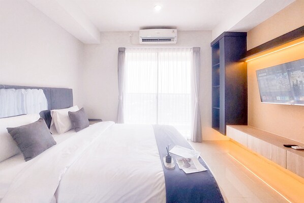 A hotel room with a large bed, a flat-screen TV mounted on the wall, and a window with curtains.