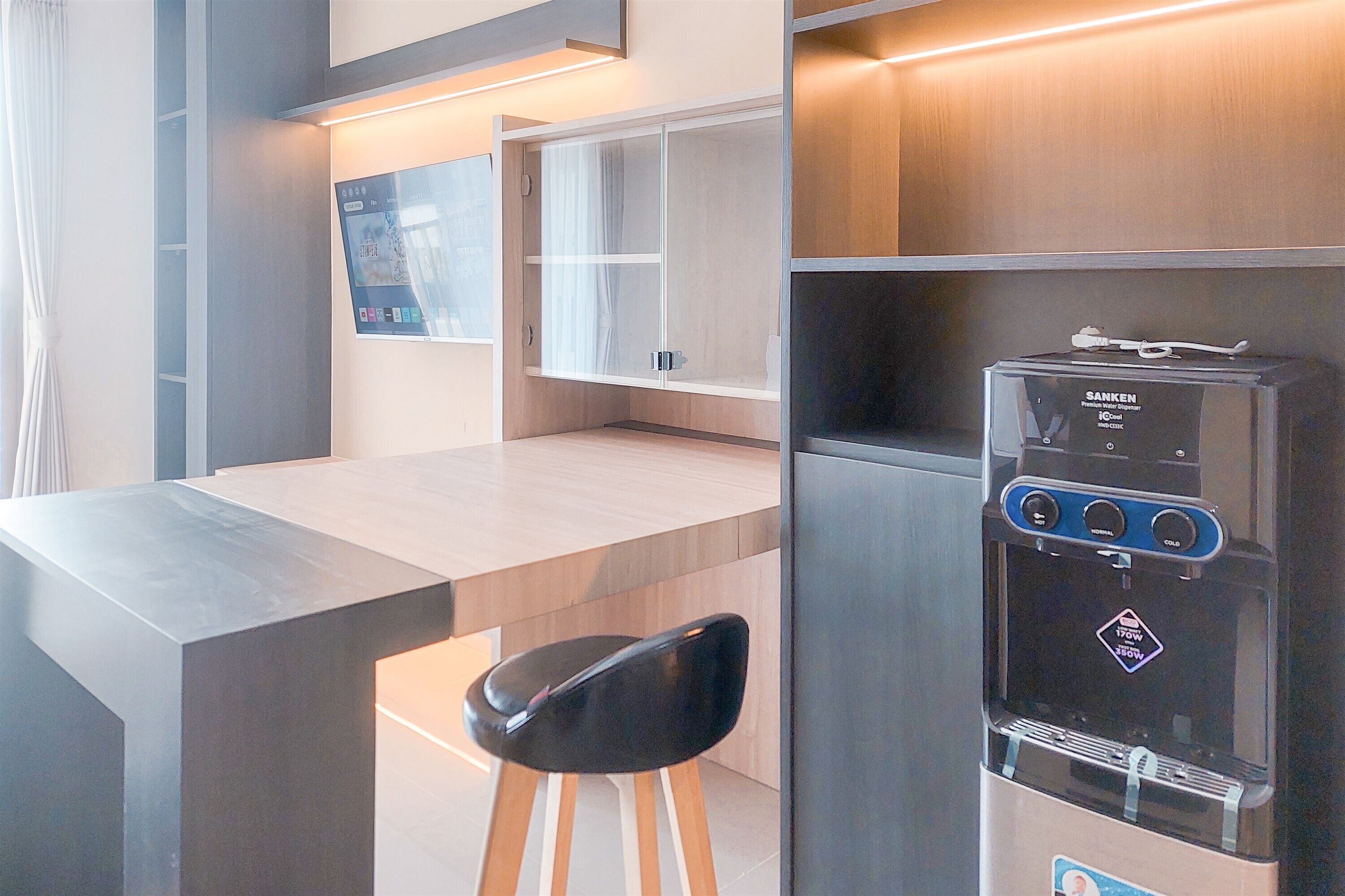 A modern kitchenette with a built-in refrigerator, a water dispenser, and a flat-screen TV mounted on the wall.