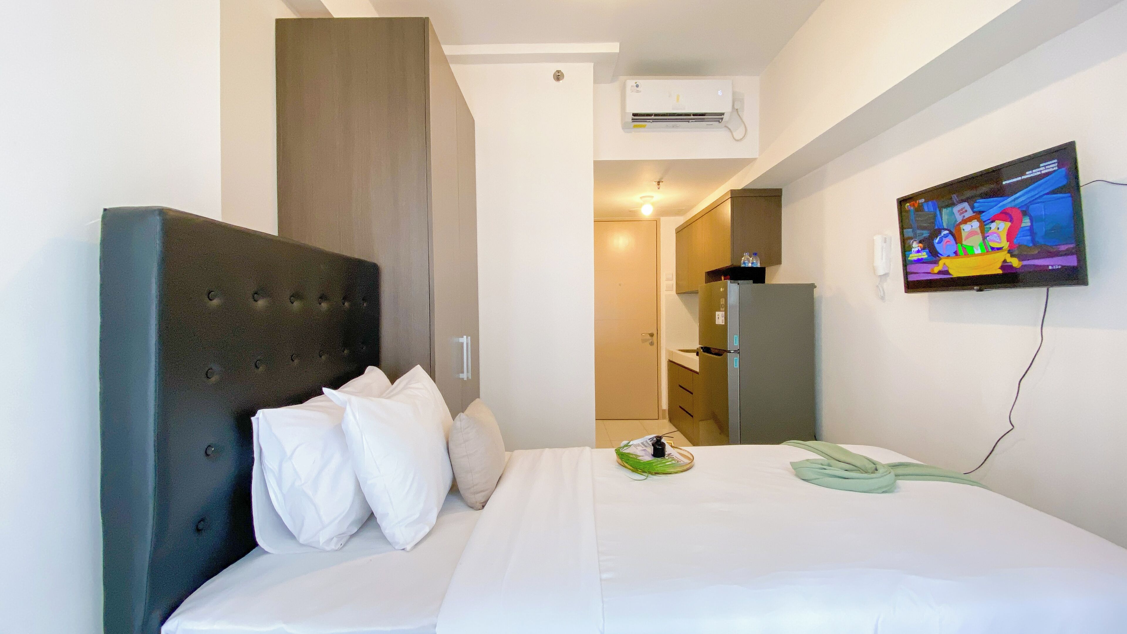 A hotel room with a bed, a television, an air conditioning unit, and a door leading to a bathroom.