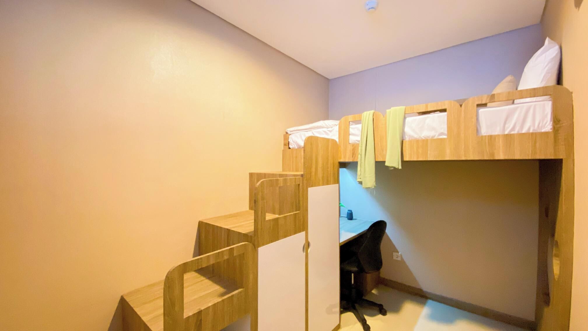 A dormitory room with bunk beds, a small desk, and a chair.