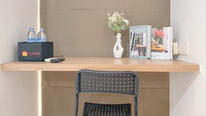Un mostrador de hotel con una silla negra, un jarrón blanco con flores, una caja de agua embotellada, un control remoto y un libro titulado 'Scandinviva Dream'.