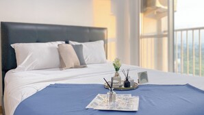 Una cama bien hecha con sábanas blancas, una colcha azul y una bandeja con un periódico, un vaso y dos velas.