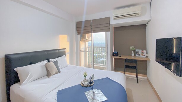 Habitación de hotel con cama, escritorio, silla, televisor y balcón con vistas.