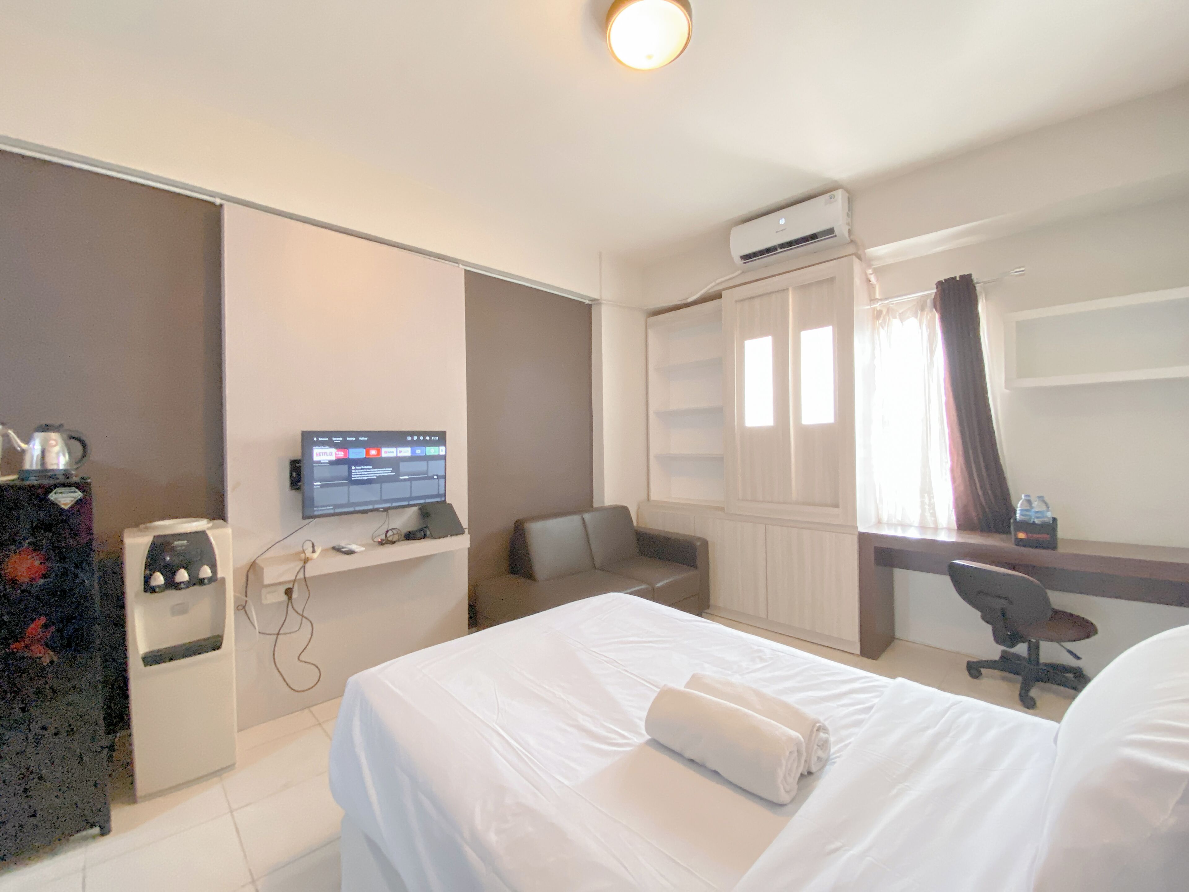 A hotel room with a bed, a desk, a chair, a television, and an air conditioning unit.