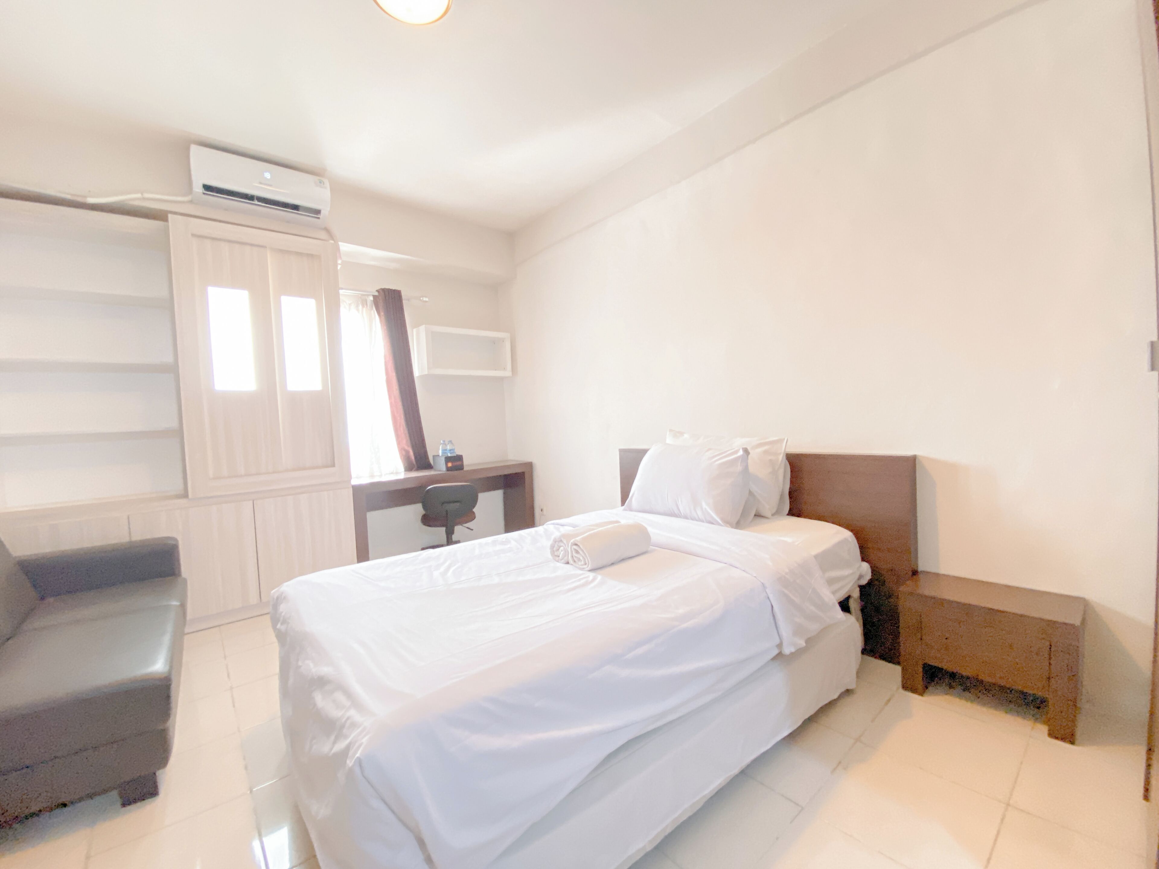 A hotel room with a bed, a desk, a chair, and an air conditioning unit.