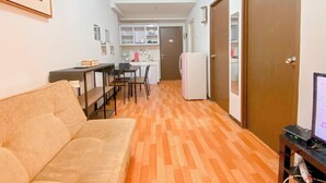 Ein kompakter Wohnbereich mit Sofa, Esstisch und Stühlen, Küchenzeile mit Schränken und Kühlschrank sowie einer Tür zu einem weiteren Raum.
