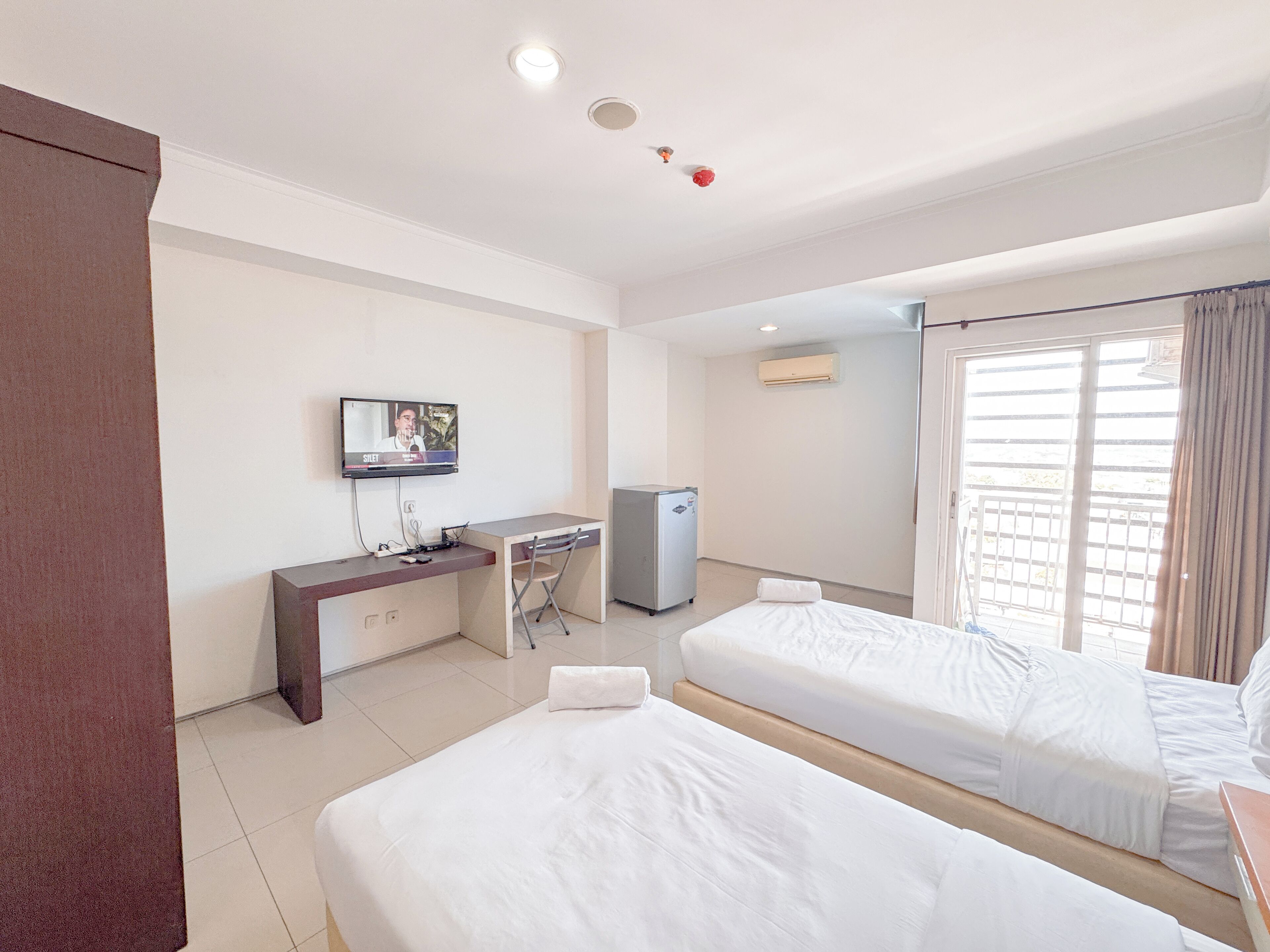 A hotel room with two beds, a desk, a television, and an air conditioning unit.