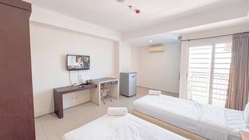 A hotel room with two beds, a desk, a television, and an air conditioning unit.