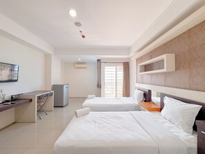 A hotel room with two beds, a desk, a television, and a minibar. - Best Price And Comfortable Living Studio At High Point Serviced Apartment (Surabaya)