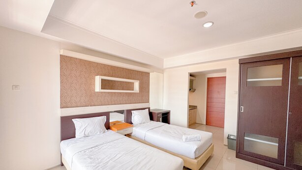 A hotel room with two single beds, a small table, a mirror, and a wardrobe. - Best Price And Comfortable Living Studio At High Point Serviced Apartment (Surabaya)