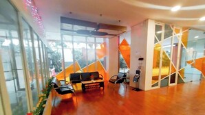 A spacious lobby with a wooden floor, a sofa, chairs, and a reception desk. - Best Price And Comfortable Living Studio At High Point Serviced Apartment (Surabaya)
