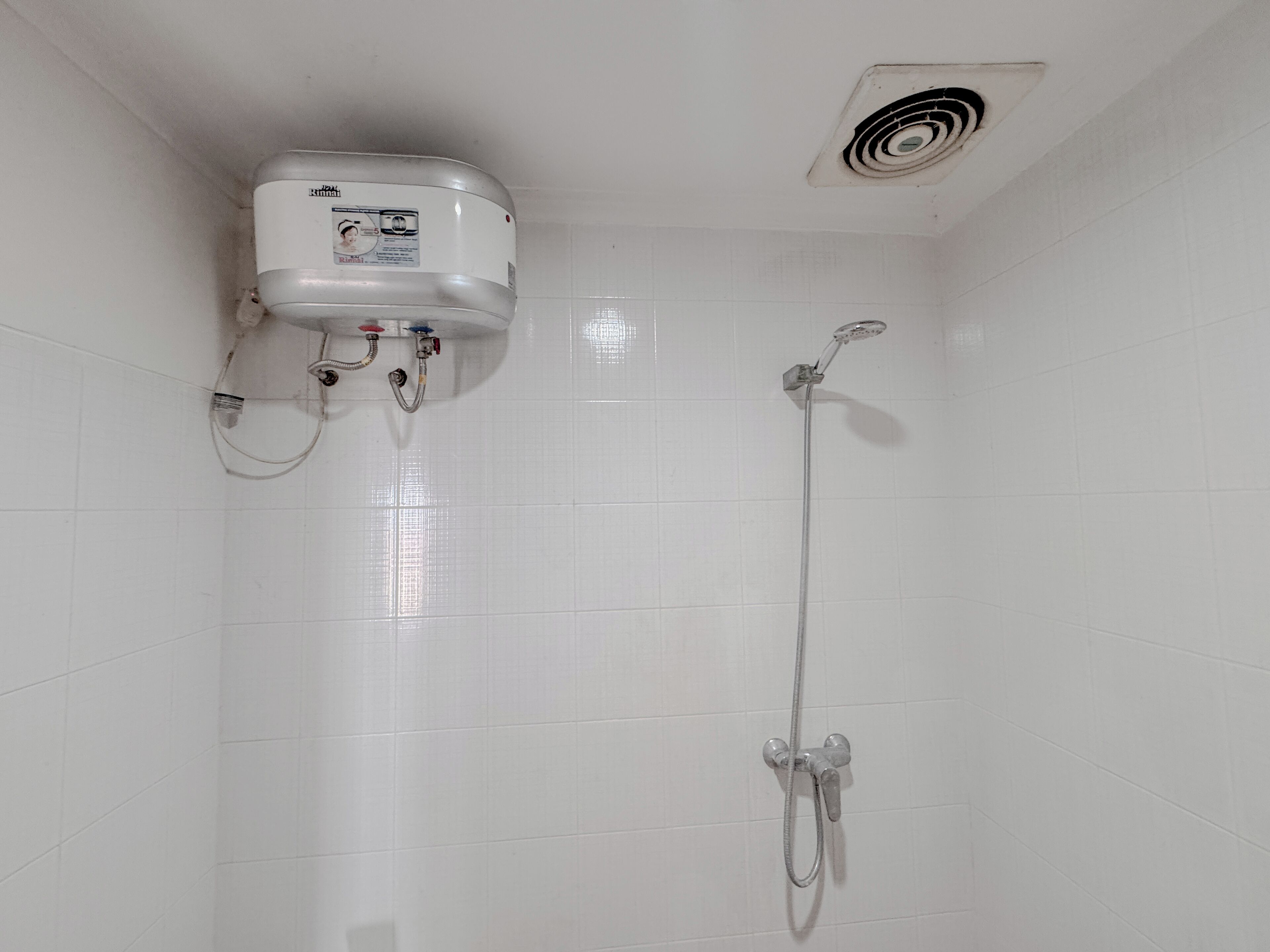 A bathroom with white tiled walls, a shower with a handheld showerhead, and a wall-mounted heater.