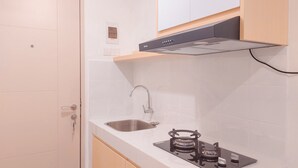 A compact kitchen with a stainless steel sink, a gas stove, and a range hood above the stove. - Best Price And Comfy Studio At Tokyo Riverside Pik 2 Apartment (Teluknaga)