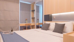 A hotel room with a large bed, a desk with a chair, a mirror, and a wardrobe. - Best Price And Comfy Studio At Tokyo Riverside Pik 2 Apartment (Teluknaga)