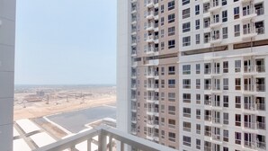 A high-rise building with multiple balconies and a view of a construction site and a body of water. - Best Price And Comfy Studio At Tokyo Riverside Pik 2 Apartment (Teluknaga)