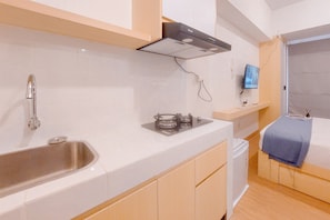 A compact kitchen with a stainless steel sink, a gas stove, and a built-in oven. There is a small shelf with a television and a power outlet. - Best Price And Comfy Studio At Tokyo Riverside Pik 2 Apartment (Teluknaga)