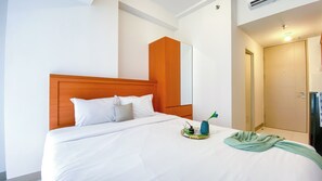 A hotel room with a bed, a mirror, a door, and a small table with a vase and a bottle.
