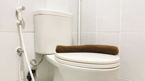 Eine Toilette mit einem braunen Handtuch auf dem Sitz, einem weißen Toilettenpapierhalter und einer weißen Rohrleitung.
